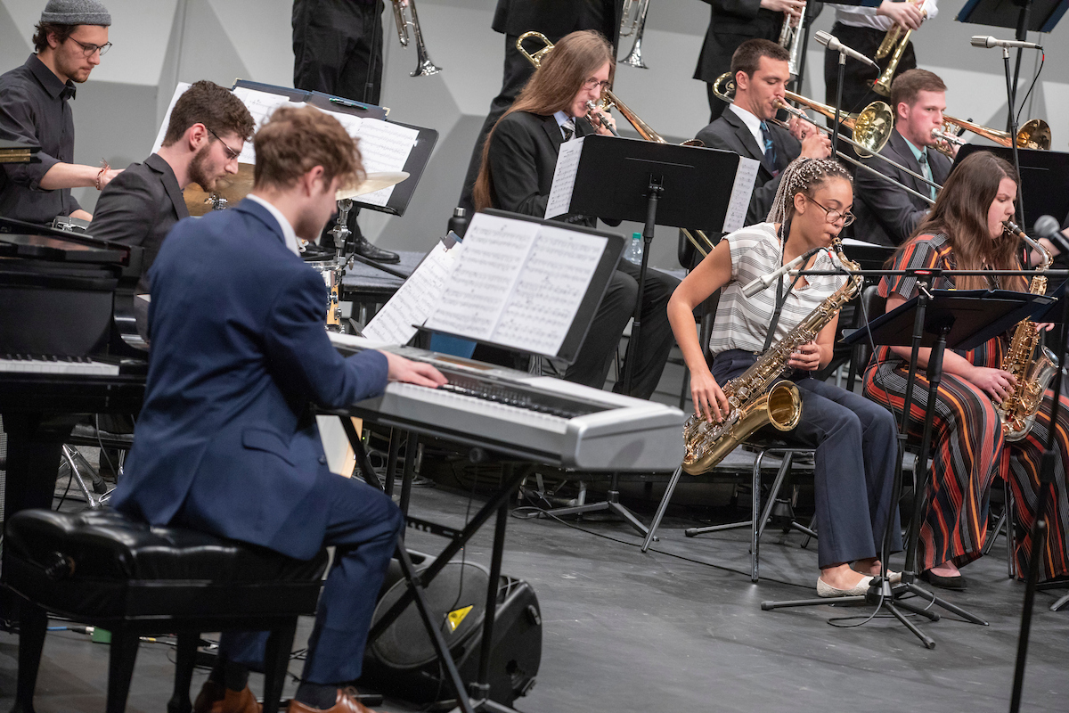 A jazz band performs on stage, featuring musicians playing keyboards, saxophones